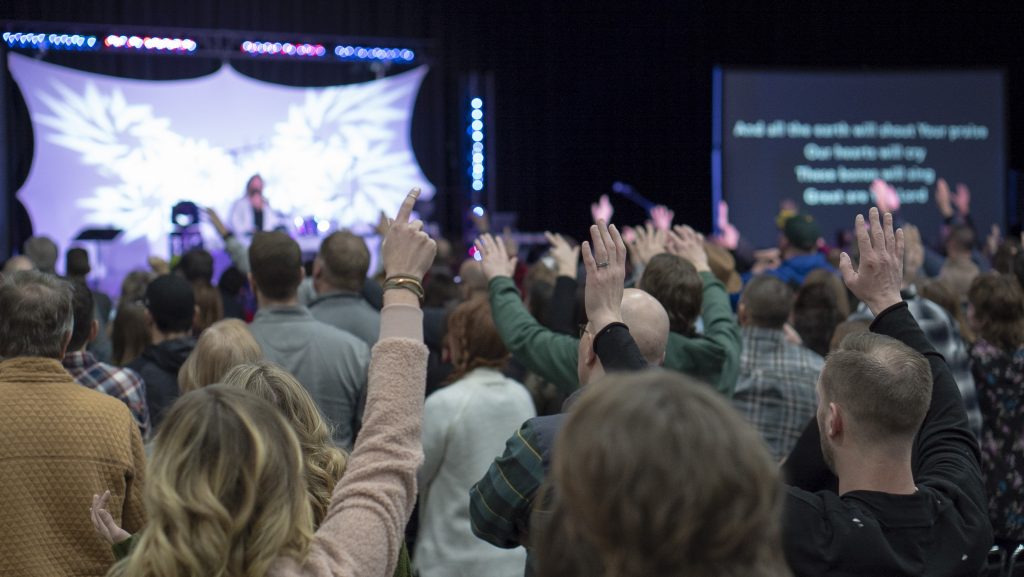 People with hands raised worshiping along with musicians